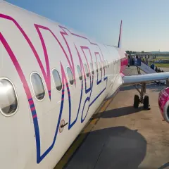Samolot Wizz Air z widocznym logo, pasażerowie wsiadają po schodkach.