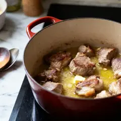 Morceaux de veau dorés mijotant dans une cocotte rouge, prêts pour un savoureux sauté de veau grand-mère. Une touche de beurre ajoute à la richesse.