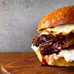 Saftiger pulled beef burger mit geschmolzenem Käse und BBQ-Sauce, serviert auf einem Holzbrett.