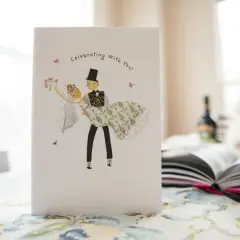 Kartka z weselem, jakby z nieznanych wierszy o miłości. Pan młody niesie pannę młodą, a napis głosi "Celebrujemy z Tobą!".