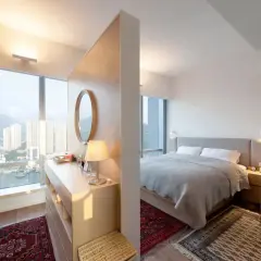 Ein moderner Schlafbereich mit einem Bett, getrennt durch einen eleganten raumteiler vorm bett, der auch als Schminktisch dient.