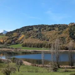 El estany de Montcortès, un espejo de agua sereno rodeado de colinas otoñales y un cielo azul claro.