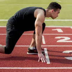 Mężczyzna w pozycji startowej na bieżni. Czy bieganie jest zdrowe? Ten sportowiec z pewnością tak uważa, gotowy do sprintu.