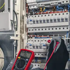 Ein Elektriker prüft mit einem Multimeter eine Schalttafel. Das Bild zeigt die sorgfältige Arbeit, die für ein gutes industrieelektriker gehalt wichtig ist.