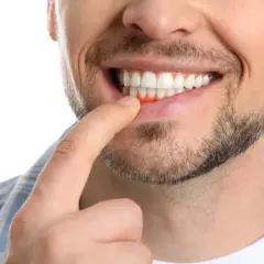 Mężczyzna wskazuje palcem na swoje zaczerwienione, krwawiące dziąsła.