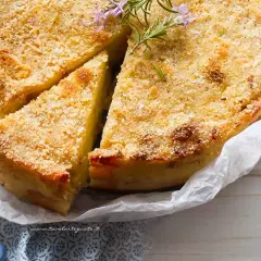 Delizioso gateau di patate dorato e croccante, guarnito con rosmarino fresco. Una fetta è già stata tagliata, invitando ad assaporare questo piatto.