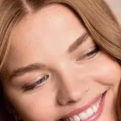 Sonrisa radiante de una mujer con marron ceniza pelo, ojos azules y piel luminosa.