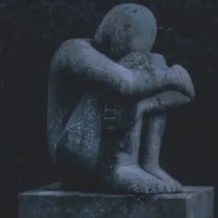 Eine traurige Steinstatue, die sich in sich zusammenkauert, symbolisiert das schlechte Gewissen nach dem Tod des Partners.