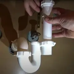 Hands assemble a white P-trap for a kitchen sink installation.
