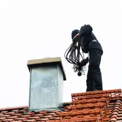 Kominiarz na dachu przygotowuje się do wypalania komina, trzymając szczotkę i liny.
