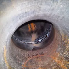Widok wnętrza rury z widocznym, nierównym, zimnym spawem. Rdza i naloty na metalowej powierzchni.