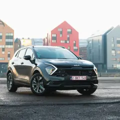 Czarny, mały SUV Kia Sportage stoi na mokrym asfalcie przed nowoczesnymi budynkami.