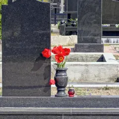 Cmentarz z nagrobkami z czarnego granitu, wazon z czerwonymi tulipanami i znicz.