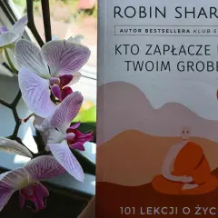Delikatne storczyki obok książki "Kto zapłacze nad twoim grobem" Robina Sharmy, autora bestsellerów.