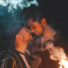 Coppia gay che si bacia con scintille e fumo, un momento intimo e passionale.