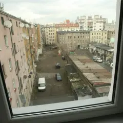 Podwórko kamienicy z satelitami na ścianach. Widać samochody i garaże. Trudno ocenić, ile metrów na osobę mieszkanie komunalne.