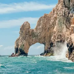 Un paseo en barco revela el Arco de Cabo San Lucas, una maravilla natural que ver en Baja California. Las olas rompen contra las rocas doradas bajo un cielo azul.