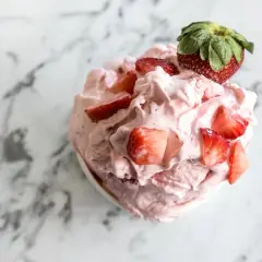 Un délice rose et crémeux : un sorbet fraise garni de morceaux de fruits frais et d'une fraise entière sur un fond marbré.
