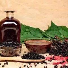 Wino z czarnego bzu przepis: butelka ciemnego płynu, miseczki z owocami i liśćmi czarnego bzu, gotowe do przygotowania domowego trunku.