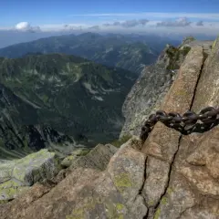 Łańcuch ułatwia wspinaczkę na skalisty świnica szczyt. W tle rozciągają się zielone pasma górskie.