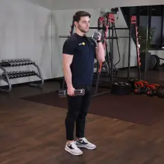 Mężczyzna wykonuje zottman curl z hantlem, ćwicząc biceps i przedramię. W tle siłownia z maszynami i ciężarami.