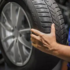 Dłoń mechanika trzymająca oponę zimową. Pamiętaj, co ile wymieniać opony zimowe, by zapewnić bezpieczeństwo.