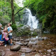 Familia toma selfie frente a la imponente cascada Xorroxin, rodeada de exuberante vegetación y rocas.