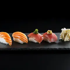 Sashimi-Nigiri mit Lachs und Thunfisch auf schwarzem Schiefer, daneben eingelegter Ingwer.