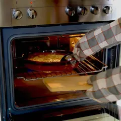 Mit Ofenhandschuhen wird ein Auflauf aus dem Backofen mit Umluft genommen.