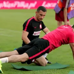 Remigiusz Rzepka pomaga piłkarzowi w ćwiczeniach na murawie.