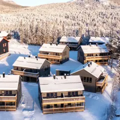 Vinterlandskap med snötäckta hus i Funäsdalens stugby. Solen lyser på de moderna stugorna och den snöklädda skogen.