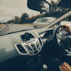 Widok z wnętrza samochodu jadącego po drodze, ręce na kierownicy.