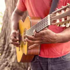 Uomo suona chitarra acustica all'aperto, ideale per imparare canzoni in inglese con testo facile.