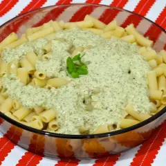 Macarrones al pesto servidos en un bol de cristal, con una hoja de albahaca fresca decorando la cremosa salsa verde.