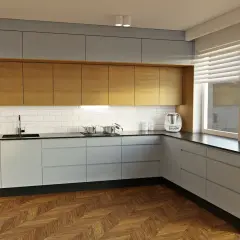 Nowoczesna kuchnia z drewnianymi frontami, szarymi szafkami i czarnym blatem. Idealne maskowanie szczelin przy meblach zapewnia czysty wygląd.