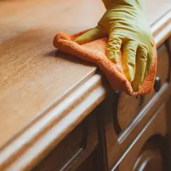 Ręka w żółtej rękawiczce czyści drewnianą komodę pomarańczową ściereczką. Dowiedz się, czym rozpuścić klej, by usunąć uporczywe plamy.
