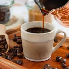Frisch aufgebrühter türkischer Mokka fließt in eine Tasse. Kaffeebohnen liegen auf einem Holztablett.