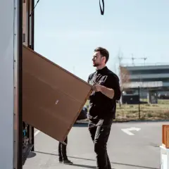 Man packar tavlor för flytt. Han bär en stor, platt kartong mot en lastbil.