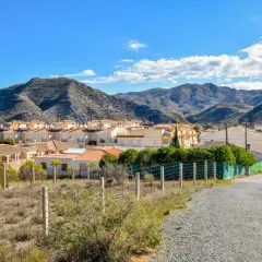 Casas blancas y tejados naranjas bajo montañas áridas en Los Lobos, Almería. Un camino de grava serpentea hacia el pueblo.