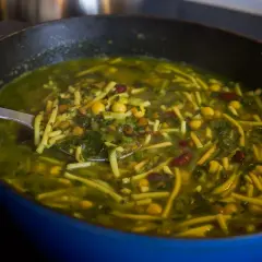 En skål med grön, mustig ash reshte-soppa med nudlar, linser, kikärtor och bönor.