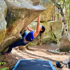 Kobieta wspina się po skale w lesie, doświadczając emocji związanych z boulderingiem w Fontainebleau.