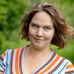 Underbara Claras leende möter kameran i en randig klänning, med en lummig skog i bakgrunden.