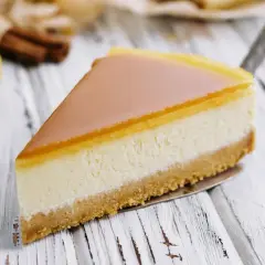 Kawałek najdelikatniejszego sernika z mascarpone na zimno z błyszczącą polewą, na tle cytryny i cynamonu.