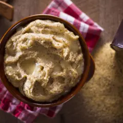 Polenta taragna cremosa servida en cuenco de barro, con queso y maíz esparcido alrededor.