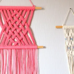Deux tentures murales en macramé : une rose vif avec un motif croisé, et une écru avec des perles bleues. Idéal pour un tuto macramé mural.