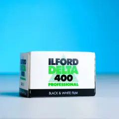 A box of Ilford Delta 400 Professional black and white film sits on a white surface against a bright blue background.