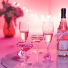 Bottiglia e calici di vino rosato, un brindisi alla vinificazione in rosato, con fiori e luci soffuse.