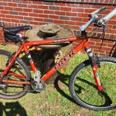 A red Trek 6500 ZX mountain bike rests on grass in front of a brick wall.