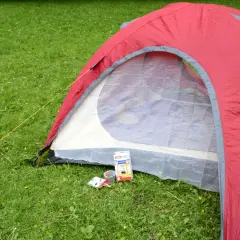 Czerwony namiot na trawie, obok taśma klejąca i zestaw do naprawy namiotów.