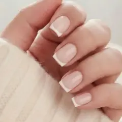 En hand med klassisk fransk manikyr på korta naglar, insvept i en mjuk, beige tröja.